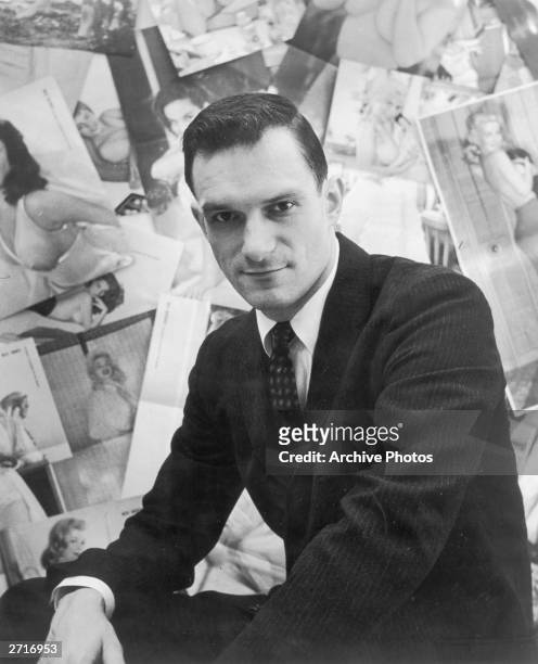 Portrait of American publisher Hugh Hefner sitting in front of a wall collage of female centerfolds from his men's magazine 'Playboy' which he...