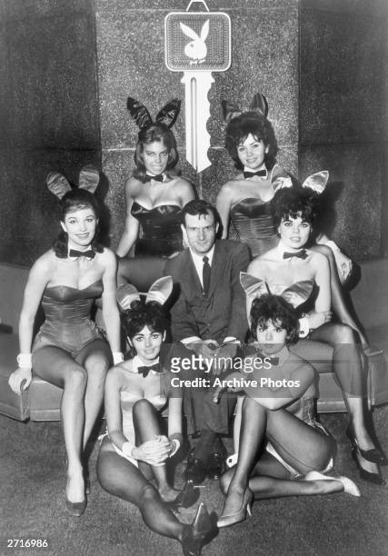 Portrait of American publisher Hugh Hefner, president of the Playboy Club and editor-publisher of 'Playboy' magazine, sits with six Bunnies who have...
