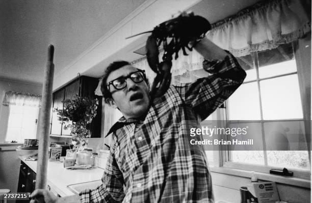 American comic actor and film director Woody Allen stands in a kitchen and recoils from a lobster he is holding with a look of fright on the set of...