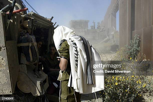 An Israeli soldier wears his prayer shawl and phylacteries as he recites his daily prayers behind Israel's steel plate security barrier between Gaza...