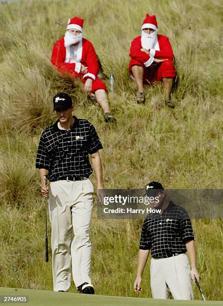 International Team members Adam Scott of Australia and Ernie Els of South Africa line up a putt in front of a pair of Santa Claus' on their way to...