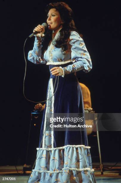 American country singer and songwriter Loretta Lynn performs on stage, wearing a long dress, circa 1980.