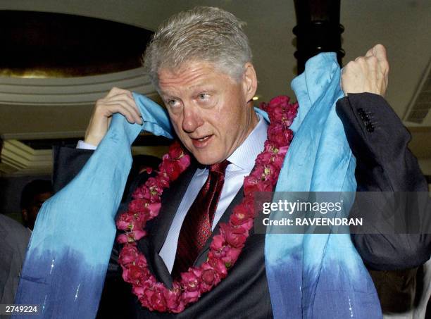 Former US President Bill Clinton adjusts his Indian shawl as he talks to the press during a breakfast meeting, in New Delhi 21 November 2003, with...