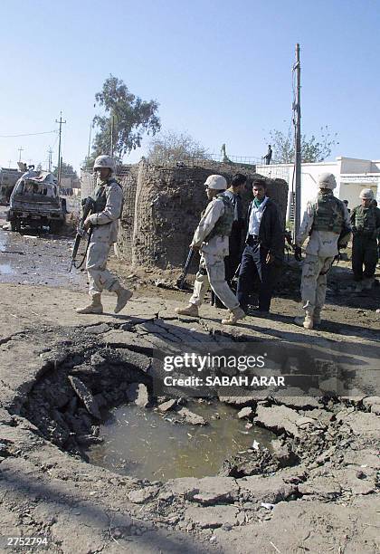 Soldiers and members of the Iraqi police walk past a crater caused by a suicide bombing that hit the police station of the small town of Khan Bani...