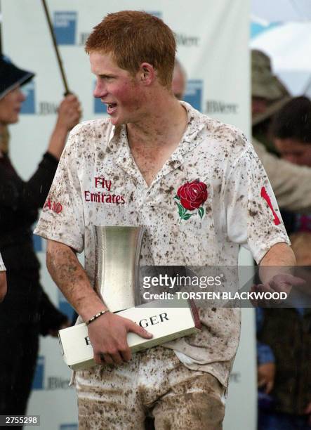 Mud splattered Britain's Prince Harry carries his trophy and a bottle of Bollinger champagne after winning the Young England vs Young Australia polo...