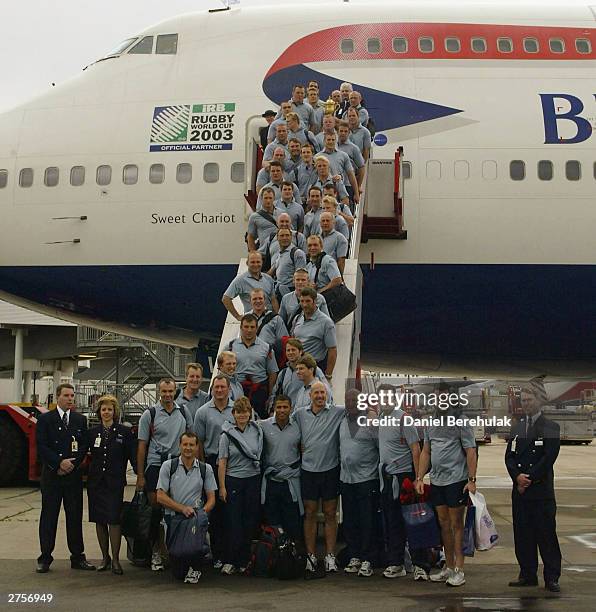 The England team hold aloft the Webb Ellis Trophy on the stairs of the British Airways BA16 aircraft during the departure of the England Rugby team...