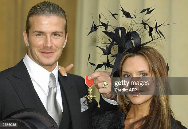 England's football captain David Beckham stands with his wife, Victoria, as he shows off the OBE he received 27 November from Britain's Queen...