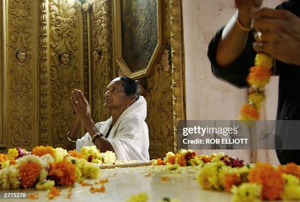 An Indian Christian worshipper raises her hands in prayer as another prepares a floral garland at the base of Saint Francis Xavier's raised pediment...