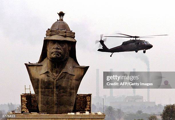 Military helicopter hover over a giant bronze busts of Saddam Hussein as workers prepare to diamantle it at the former presidential palace in Baghdad...