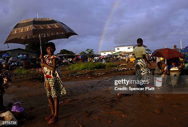 Girls stands on the roadside during a brief sun-shower September 1, 2003 in Monrovia, Liberia. Thousands of Liberians have been displaced by war and...