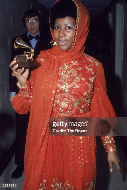 American soul singer Aretha Franklin stands backstage wearing an gold embroidered gown and holding a Grammy Award, circa 1970.