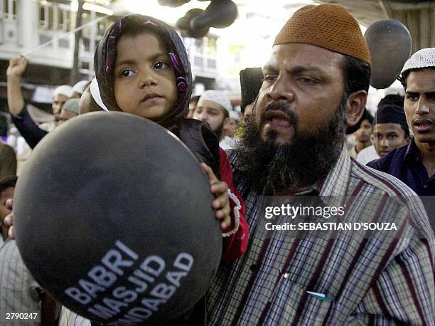 Young Muslim girl holds a black balloon with the message " Babri Masjid Zindabad " in her hands as she is carried by her father during a march along...