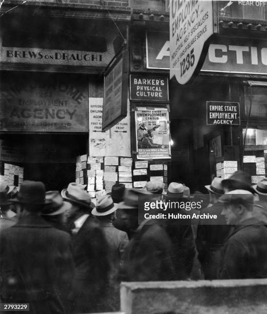 Crowed of unemployed men gather in the rain in front of a row of employment agencies on Sixth Avenue during the Great Depression, New York City, 1931.