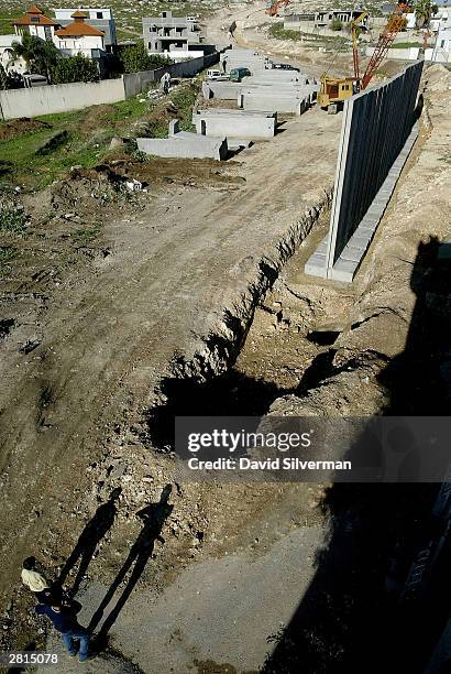 Palestinians watch as Israeli workers construct the security wall December 16, 2003 between the West Bank Palestinian village of Nazlat Issa and the...