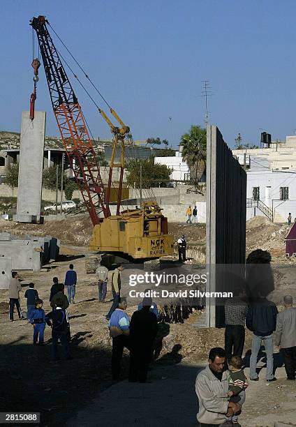 Palestinians watch as Israeli workers build the security wall December 16, 2003 between the West Bank Palestinian village of Nazlat Issa and the...