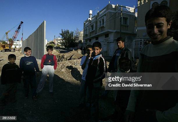 Palestinian boys gather where Israeli workers builds Israel's security wall December 16, 2003 between the West Bank Palestinian village of Nazlat...
