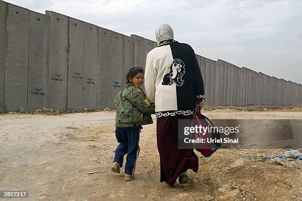 Palestinian woman and her daughter walk alongside the Israeli separation barrier December 22, 2003 between their West Bank village of Nazlat Issa and...