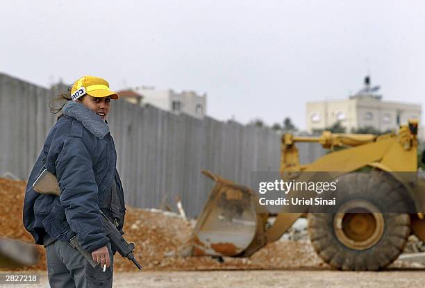 An armed Israeli woman stands guard as work continues on the Israeli separation barrier December 22, 2003 between their West Bank village of Nazlat...