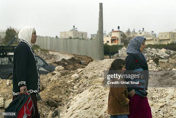 Palestinians walk through the construction site of the Israeli separation barrier December 22, 2003 between their West Bank village of Nazlat Issa...