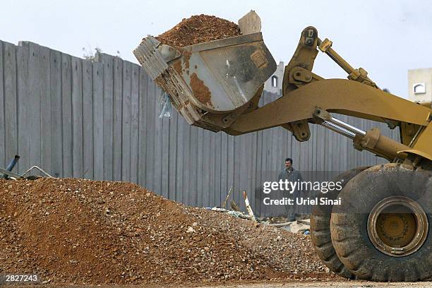Palestinian man passes a bulldozer working on the Israeli separation barrier December 22, 2003 between their West Bank village of Nazlat Issa and the...