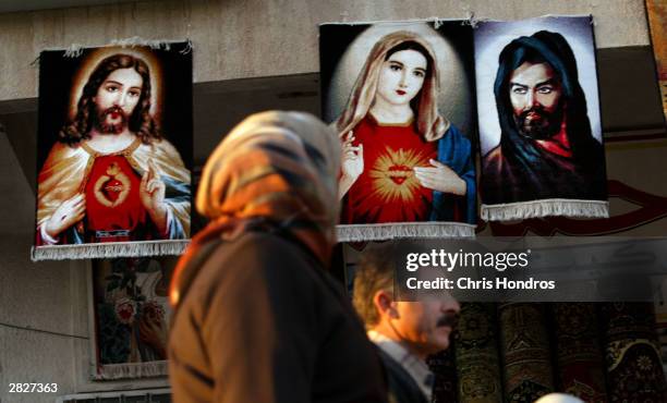 An Iraqi couple pass by rugs depicting Christian figures Jesus and Mary, as well as the founder of Shia Islam Imam Ali December 22, 2003 in Baghdad,...