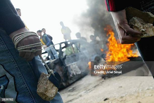 Palestinian boys with sling and rocks in hand stand by a burning car during clashes over Israel's controversial separation barrier January 1, 2004...