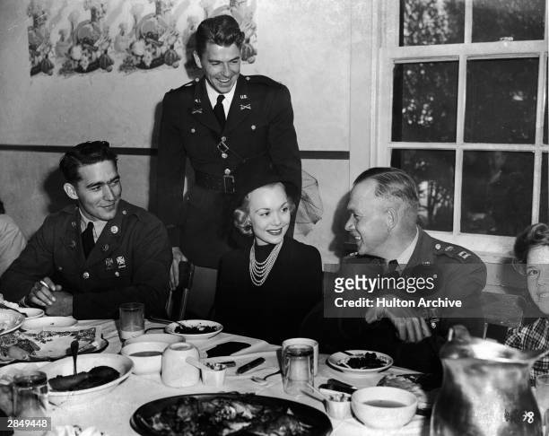 American actor and politician Ronald Reagan stands behind his wife, actor Jane Wyman, who sits down to dinner, circa 1940s. She is seated between two...