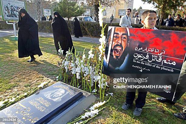 Iranian women walk past as a boy holds a placard near a newly laid tombstone to honour Khaled Eslamboli, the assassin of former Egyptian president...