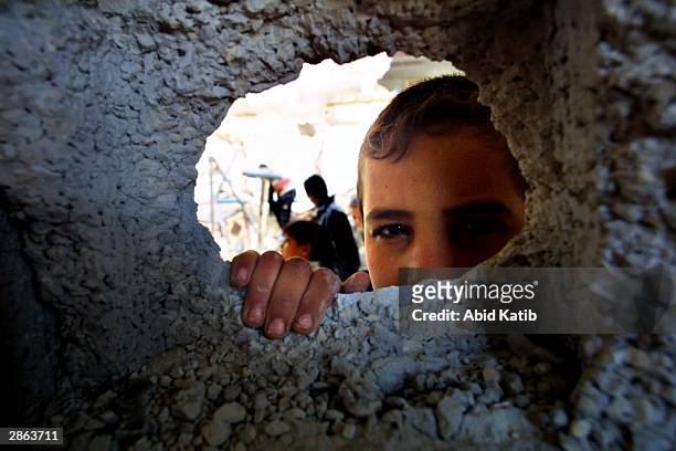 Palestinian child peers through a hole in the wall as other Palestinians inspect the rubble of their destroyed homes January 13, 2004 in Rafah...