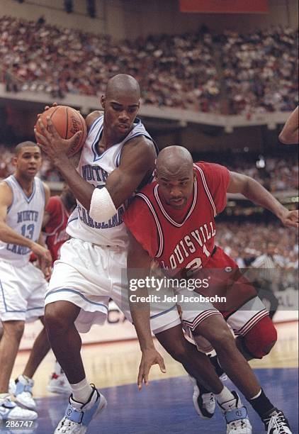 Guard Antawn Jamison of the North Carolina Tarheels holds the ball as forward Nate Johnson of the Louisville Cardinals falls over him during a...