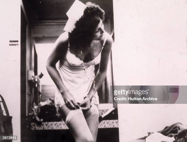 American actor Linda Lovelace removes her stocking, wearing a slip and a nurse's hat in a still from the film, 'Deep Throat,' directed by Gerard...