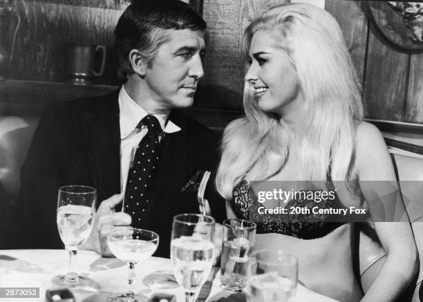 American actor Edy Williams speaks to an unidentified man at a restaurant table, wearing only a bra, in a still from the film, 'The Secret Life of An...