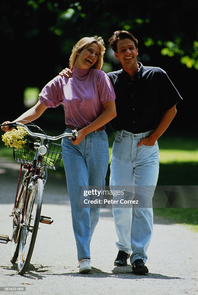 Couple wearing jeans in park,woman pushing bicycle,flowers in basket