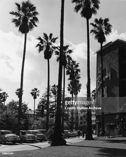 Exterior view of the landmark Beverly Hills Hotel with tall palm trees and cars parked in front of the hotel, California, circa 1950s.