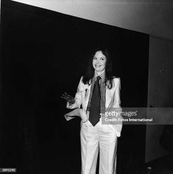 American actor and director Diane Keaton poses with a big smile and tilted head at the 48th Academy Awards and wears a white suit with a carnation in...