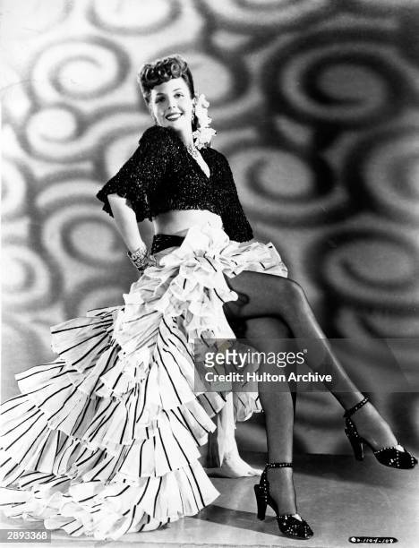 Portrait of American actor and dancer Ann Miller as she sits for a publicity still, circa 1950. She wears a half-length shirt, a tiered, ruffled...