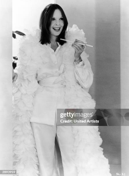 American actor Diane Keaton wears a white satin outfit with a matching feather boa and carries a cigarette holder in a scene from 'Sleeper,' directed...