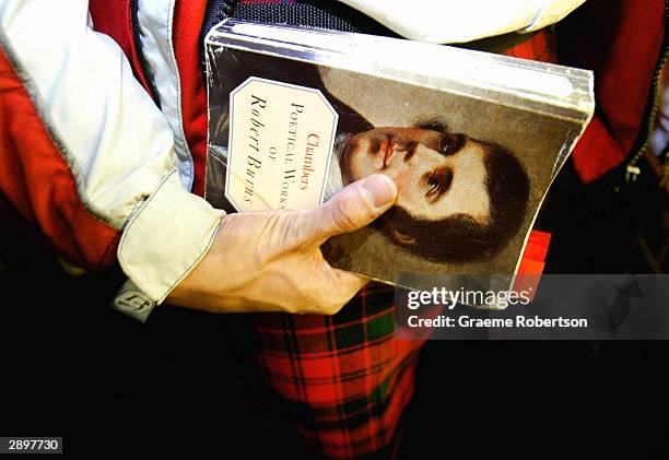 Man with traditional Scottish tartan holds a book with Robert Burns face on it at Burns Night January 24, 2004 in London, England. Scots across the...