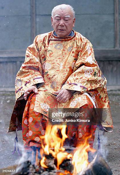 Man, dressed as the god, Ebisu, warms himself by a fire outside a shrine in Kamikagemori as part of the celebrations for Setsubun or the end of...