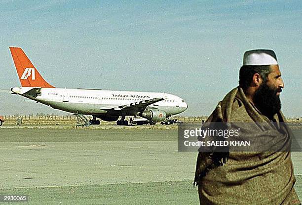 In this picture taken 28 December 1999, an Afghan man walks on the runway as an aircraft of Indian Airlines hijacked by Islamic Kahsmiri militants...