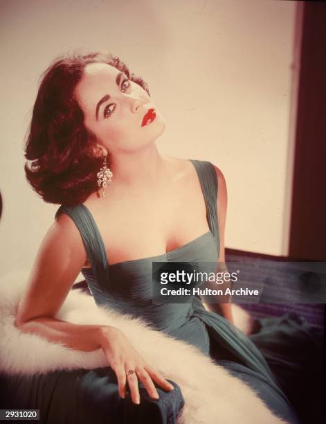 Portrait of British-born actor Elizabeth Taylor in a form-fitting green dress as she sits with her head tilted back exposing her neck, circa 1950s.