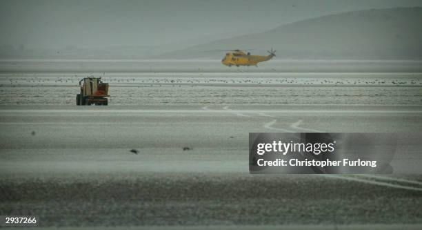 Rescue helicopter searches the sands for a group of Chinese cocklers that were stranded at sea as local workers drive a tractor on February 6, 2004...