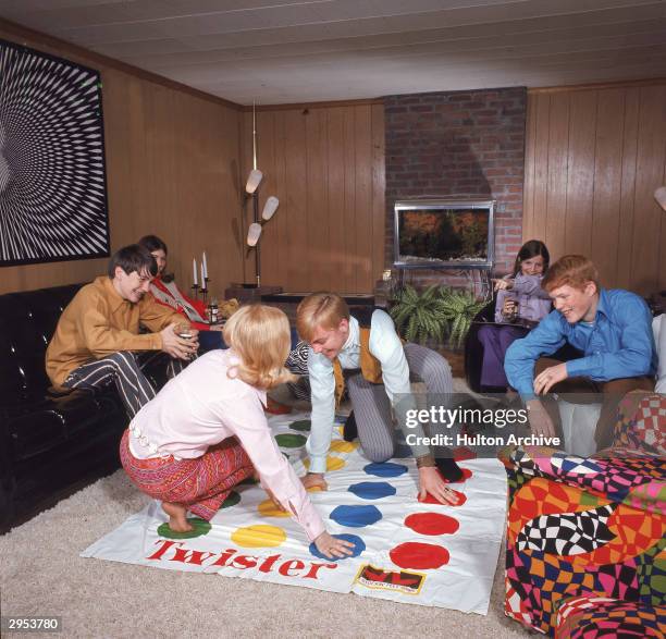 Boy and girl play the game Twister, as other young people watch in a paneled living room, circa 1968.