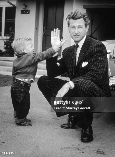 American actor Lloyd Bridges crouches in his driveway with his hand raised while his young son, Jeff, hands him a toothbrush outside their home, Los...