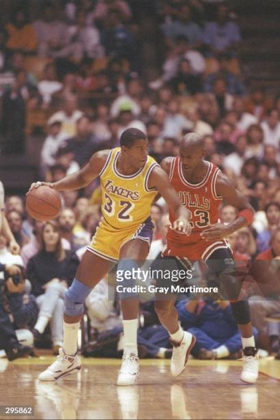 Guard Earvin Magic Johnson of the Los Angeles Lakers dribbles the ball as guard Michael Jordan of the Chicago Bulls defends him during a game on...
