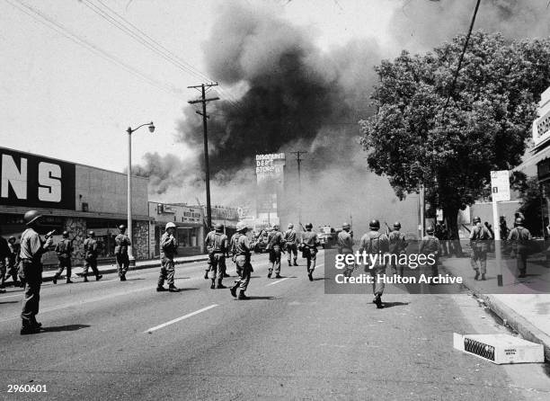 Armed National Guardsmen march toward smoke on the horizon during the street fires of the Watts riots, Los Angeles, California, August 1965.