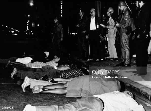Armed police stand by as rioters lie face down in the street during the Watts race riots, Los Angeles, California, August 1965.