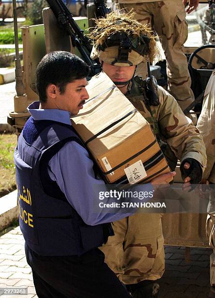 Army Sgt. Jeff Mann from the 1-22 Battalion, 4th Infantry Division hands a box of Glock 9mm handguns to an Iraqi police officer outside the...