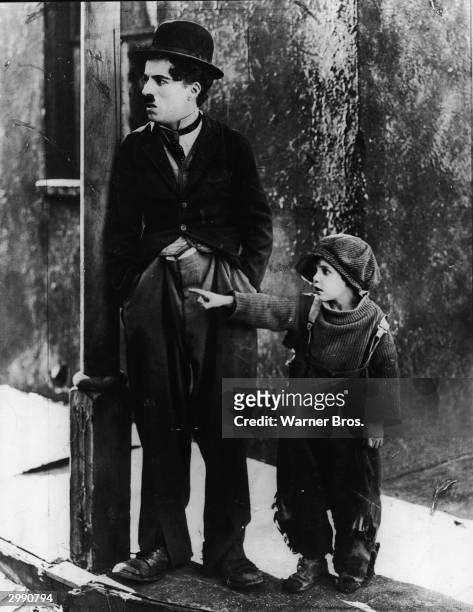 British actor Charlie Chaplin and American actor Jackie Coogan stand on a pavement by a lamp post in a still from the film 'The Kid', directed by...