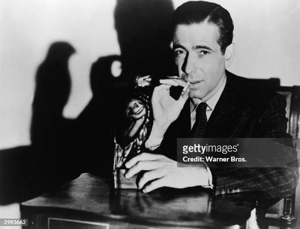 Promotional portrait of American actor Humphrey Bogart holding 'The Maltese Falcon' while smoking a cigarette, in the film directed by John Huston,...